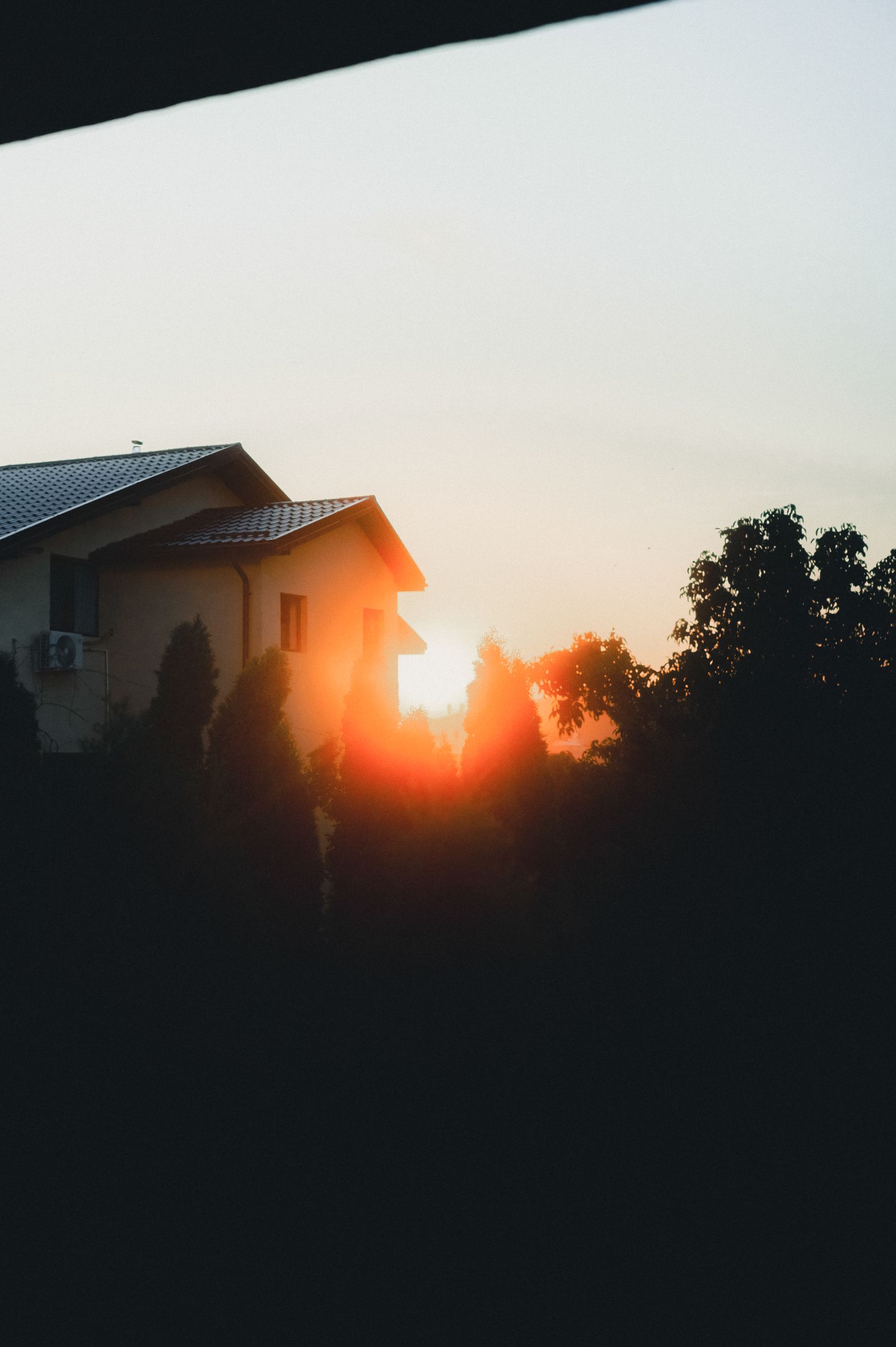 The sun coming up behind the roofline of a house
