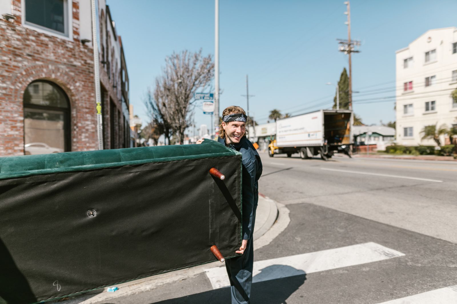 A mover carrying a large couch across a sunny street