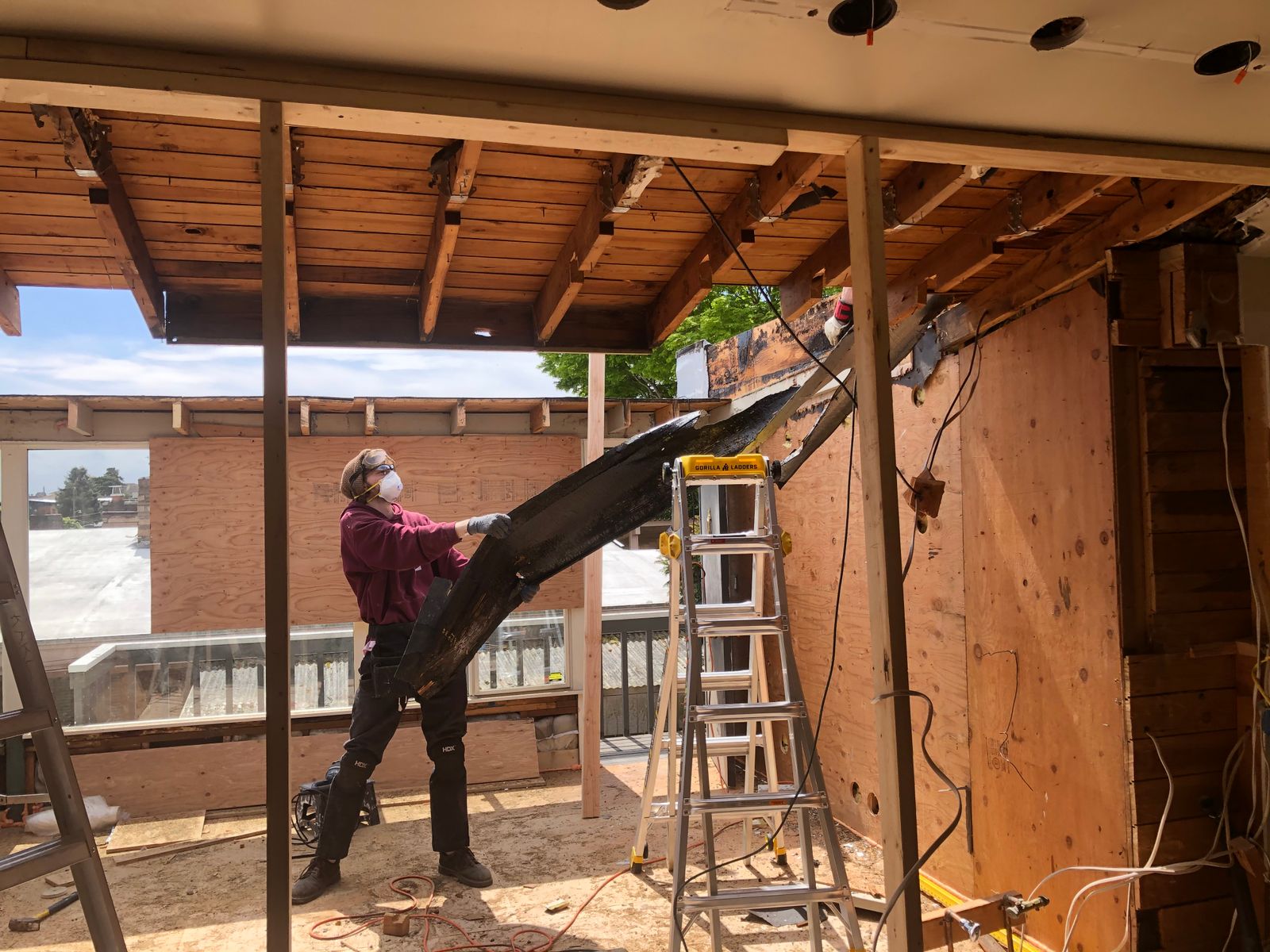 A worker in a mask pulling down framing in a partly demolished house