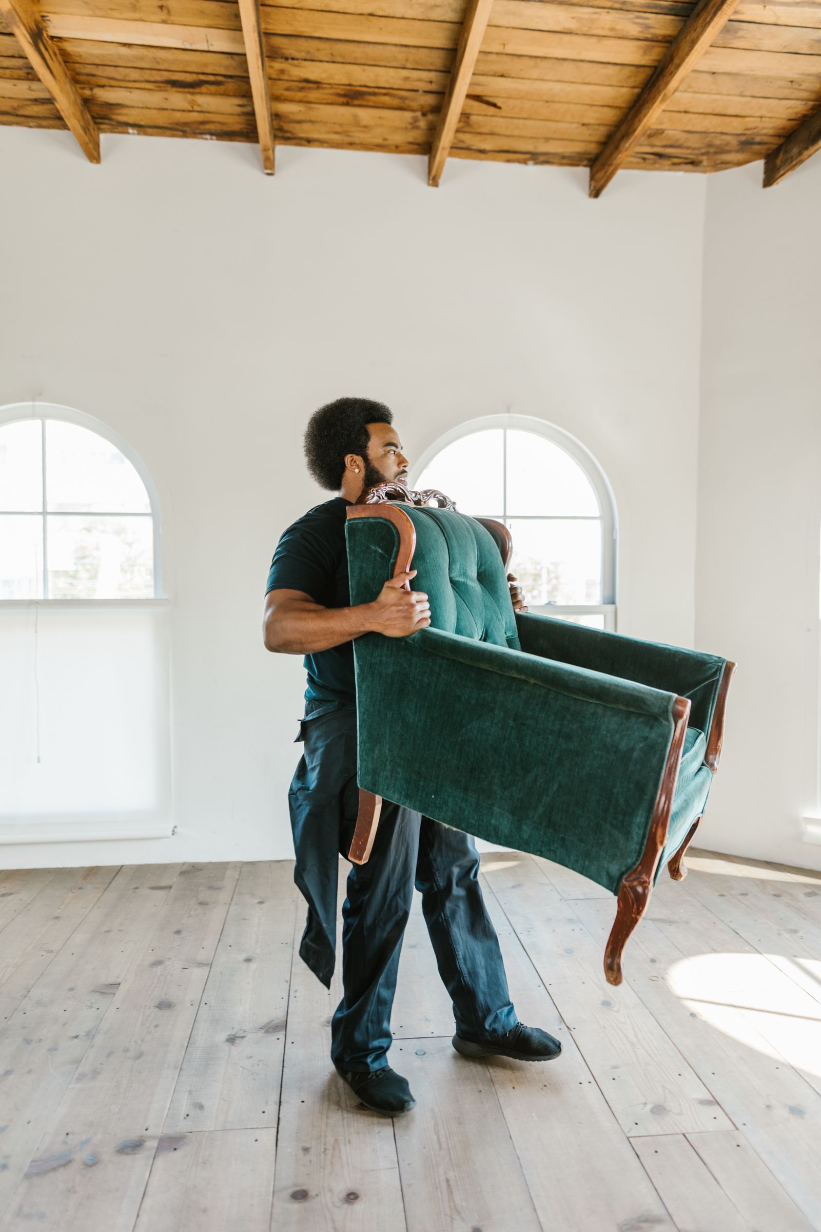 A man carrying an armchair out of a bright, empty room